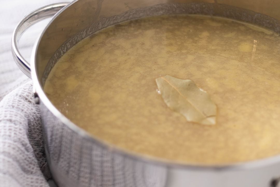 A close up of chicken broth in a large pot with a bay leaf on top